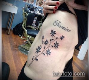 Фото тату: черная татуировка в виде ветки с листьями и надписью 'Jasmine' на боку женщины. Изящный и стильный рисунок татуировки.