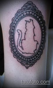 Простая черно-белая татуировка на бедре с изображением силуэта кошки, сидящей в круглой рамке с точечным узором. Минималистичный дизайн.