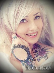 Фото девушки с татуировками на руке, плече и шее. Изображение выполнено в мягких тонах с акцентом на красоту лица и татуировок.