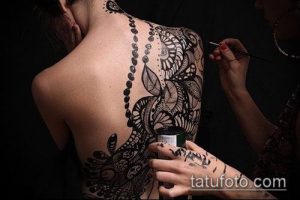 Фото тату: сложный узор в стиле кружева, выполненный черными чернилами на женской спине. Детализированный рисунок татуировки с плавными линиями и тонкими элементами.