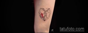 Стильная татуировка на предплечье, изображающая сердце, выполненное в геометрическом стиле. Черные линии образуют сложную структуру, а красная точка символизирует центр.