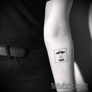 Фотография небольшой татуировки на предплечье, изображающей НЛО в квадратной рамке. Простой и загадочный рисунок татуировки.
