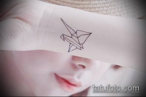 Черно-белое фото татуировки на запястье с изображением птицы, сложенной в технике оригами.