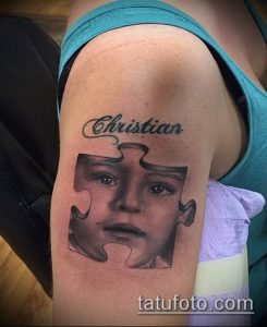 Фото тату пазла с реалистичным портретом ребенка и надписью 'Christian'. Черно-белый рисунок татуировки на плече.