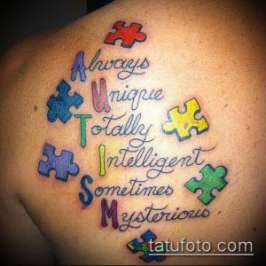 Фото тату: красочный пазл с надписью 'Always Unique Totally Intelligent Sometimes Mysterious' на плече, символизирующий аутизм.