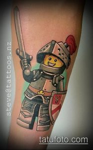 Фото тату в стиле LEGO с изображением рыцаря с мечом и щитом. Яркий и красочный рисунок на руке.