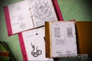 Фотография старинной книги с эскизами сак янт татуировок, изображающими змей, геометрические узоры и тайские символы.