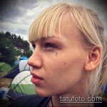 Фото тату на лице девушки: маленькая черная слеза под глазом. Изящный и минималистичный рисунок татуировки, подчеркивающий индивидуальность.