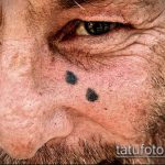 Фото тату на лице пожилого мужчины: две маленькие черные точки, имитирующие родинки. Минималистичный рисунок татуировки, создающий эффект обмана зрения.