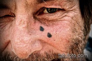Фото тату на лице пожилого мужчины: две маленькие черные точки, имитирующие родинки. Минималистичный рисунок татуировки, создающий эффект обмана зрения.