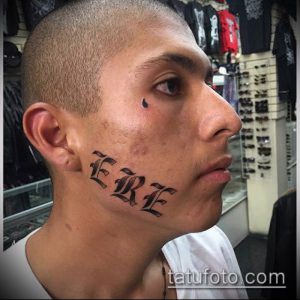 Фото тату надписи 'ERE' на щеке мужчины. Черно-белое изображение, демонстрирующее смелый и провокационный стиль.
