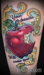 Фото татуировки на руке: красное яблоко с надписью 'Your dreams will come true', окруженное золотыми завитками. Мотивационная татуировка с ярким дизайном.