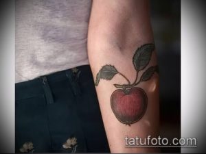 Фото татуировки с изображением красного яблока и зеленых листьев на руке. Классический и элегантный рисунок татуировки.