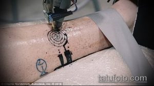 Фото процесса создания татуировки: на руке нанесен эскиз в виде спирали и рыбки, мастер начал работу с использованием тату-машинки.