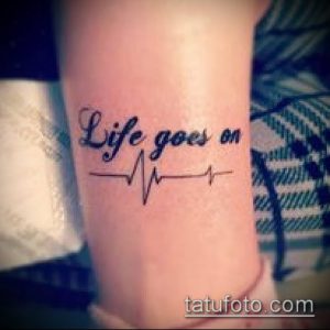 Фото татуировки с надписью 'Life goes on' и изображением кардиограммы на руке. Минималистичный черно-белый рисунок.
