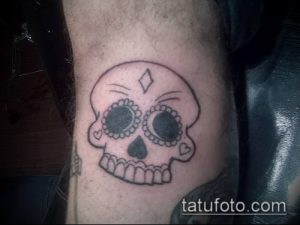 Фото тату на локте: красочный рисунок черепа в стиле сахарного черепа (sugar skull) с цветочными узорами. Традиционный мексиканский рисунок татуировки.