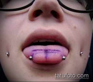 Фото пирсинга языка: два прокола с украшениями и рисунок на языке. Крупный план, акцент на цвете и форме.