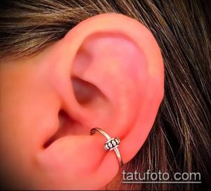 Фото пирсинга уха с золотым кольцом, украшенным камнями. Крупный план уха с акцентом на пирсинг.