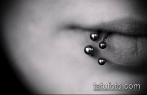 Фото тату: Крупный план нижней губы с тремя серебристыми пирсингами. Минималистичный дизайн, акцент на симметрии и аккуратности.