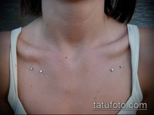 Фото пирсинга ключицы с четырьмя серебристыми украшениями и голубыми камнями. Идеально для тех, кто ищет идеи для изящного и женственного пирсинга.