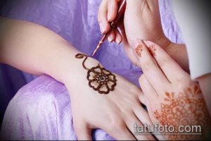 Фото процесса нанесения тату мехенди на запястье. Видна рука мастера, наносящего узор хной, и рука с уже нанесенным рисунком.
