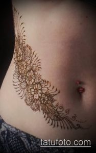 Фото тату мехенди на животе, изображающее сложный кружевной узор с цветочными мотивами. Рисунок выполнен в коричневых тонах.