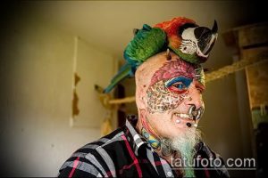 Фото мужчины с татуировкой на лице и двумя попугаями на голове. Яркие цвета, необычный стиль, смелый образ. Идеи для тату.