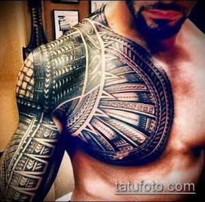 Фото татуировки: сложный узор в стиле маори покрывает грудь, руки и плечи мужчины, выполненный в черном цвете с использованием геометрических форм и спиралей.
