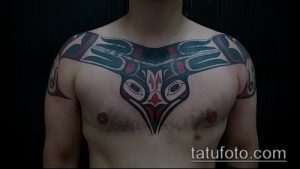 Фото татуировки на груди и плечах в стиле северо-западного побережья. Использованы черные, красные и синие цвета для создания сложного орнамента с изображением головы животного.