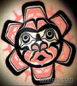 Фото тату на руке: стилизованное лицо в технике Northwest Coast Native Art с черными контурами и розовыми акцентами.