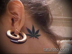 Фото тату за ухом: Небольшой лист марихуаны, выполненный в минималистичном стиле с использованием черных чернил. Деликатный и изящный рисунок татуировки.