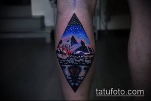 Фото тату на ноге: красивый пейзаж с горами, лесом и звездным небом, заключенный в ромб. Яркий и детализированный рисунок татуировки.