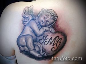 Фото тату спящего ангела, лежащего на сердце с надписью "IMG". Черно-серый рисунок татуировки с детальной проработкой лица и крыльев.
