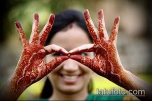 Фото тату мехенди на руках девушки, образующих форму сердца. Рисунок выполнен в красных тонах и выглядит очень жизнерадостно.