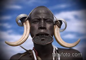 Фотография африканского мужчины с ритуальными шрамами на лице и большими серьгами-плаги в ушах.