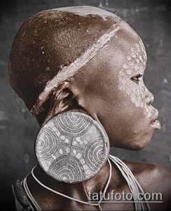 Фотография африканской женщины с традиционными украшениями, включая большие серьги-плаги и узоры на лице.