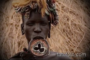 Фотография африканской женщины с традиционными украшениями и татуировкой на лице, демонстрирующая культурное наследие и красоту.