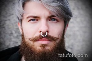 Фото мужчины с длинной серой бородой и пирсингом в носу в виде кольца. Мужчина смотрит прямо в камеру.