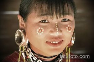 Фотография женщины с пирсингом лица: кольца в носу и ушах, точки на лице. Этнический стиль, яркие украшения.