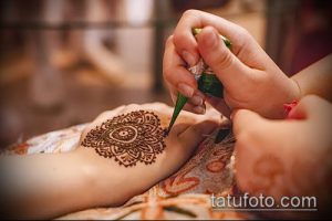 Фото процесса нанесения тату мехенди на руку. Мастер аккуратно наносит узор с помощью специальной пасты.