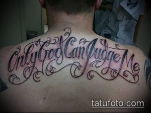 Фото тату надписи 'Only God Can Judge Me' на спине, между лопатками. Элегантный шрифт и декоративные завитки.