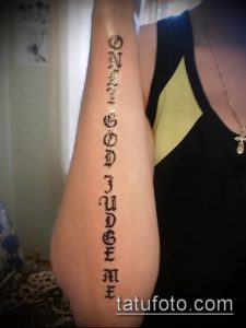 Фото тату вертикальной надписи 'Only God Can Judge Me' на руке. Черно-белый рисунок татуировки, выполненный каллиграфическим шрифтом.