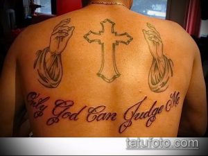 Фото татуировки на спине с изображением креста, молящихся рук и надписью 'Only God can judge me' в красных тонах.