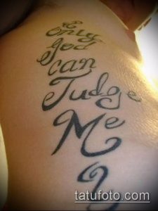 Чёрная татуировка на спине, содержащая фразу "Only God Can Judge Me", выполненную в каллиграфическом стиле с плавными линиями и завитками.