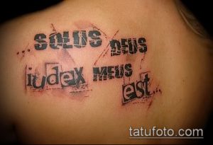 Чёрно-серая татуировка на плече с латинской фразой "Solus Deus Judex Meus Est", выполненная в стиле гранж с эффектом потёртости и брызг.