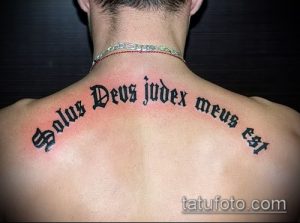 Чёрная татуировка на спине, содержащая латинскую фразу "Solus Deus Judex Meus Est", выполненную готическим шрифтом.