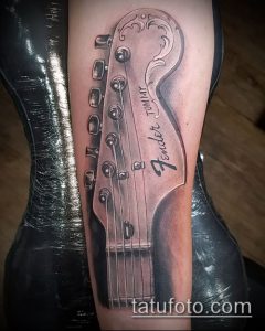 Фото реалистичной татуировки грифа гитары Fender на предплечье. Детализированный рисунок татуировки с точной передачей текстур и оттенков.