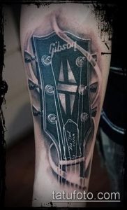 Фото тату на предплечье с реалистичным изображением головки грифа гитары Gibson. Детализированный рисунок татуировки с использованием теней и полутонов.