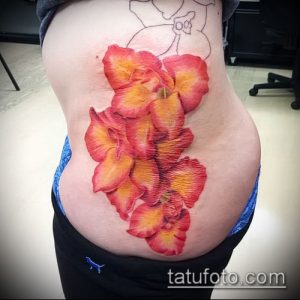 Фото тату: оранжевые и желтые гладиолусы на боку. Красочный и привлекательный рисунок татуировки.