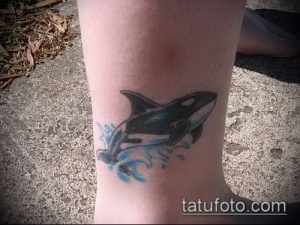 Фото тату косатки на лодыжке. Небольшой рисунок в синих тонах с изображением брызг воды, выполненный в простом стиле.
